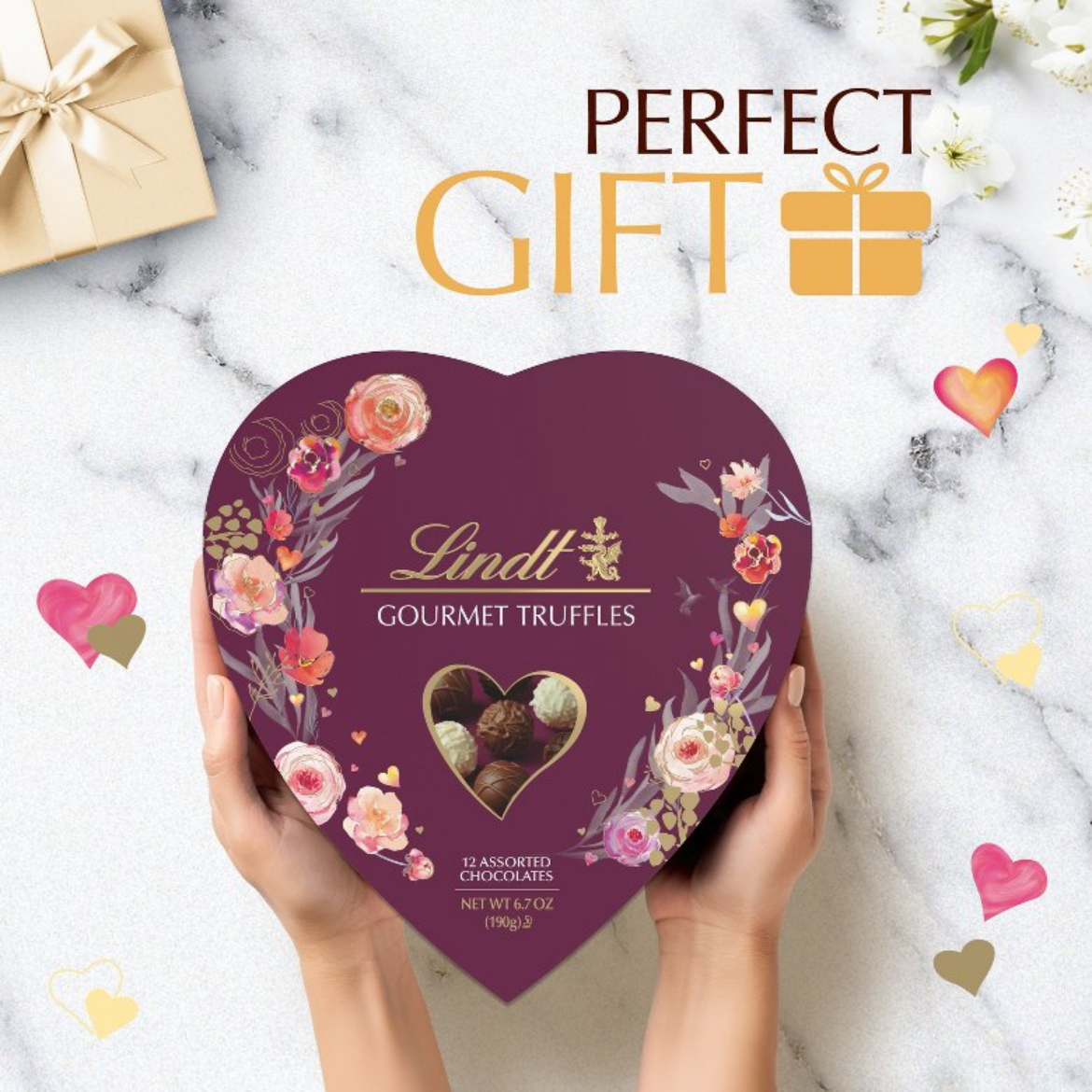 Heart-shaped Lindt chocolate box held by hands on a marble surface with 'Perfect Gift' text.