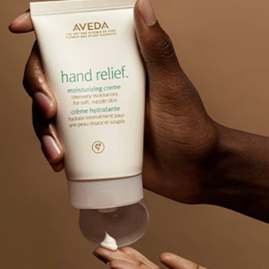 Hand holding a tube of Aveda Hand Relief moisturizing crème with visible cream on the palm.