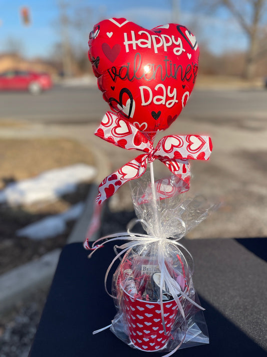 Valentine's Day-themed balloon and gift set on a table outdoors.