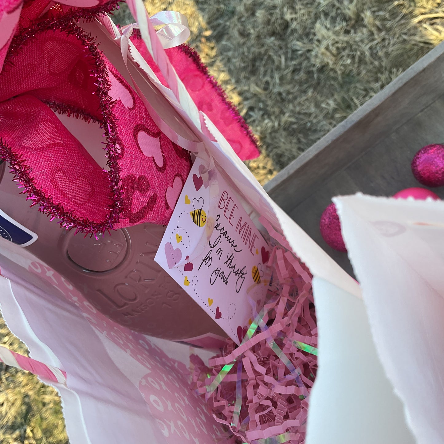 Pink tinsel-edged bow with heart details and an enclosure card attached to a gift bag
