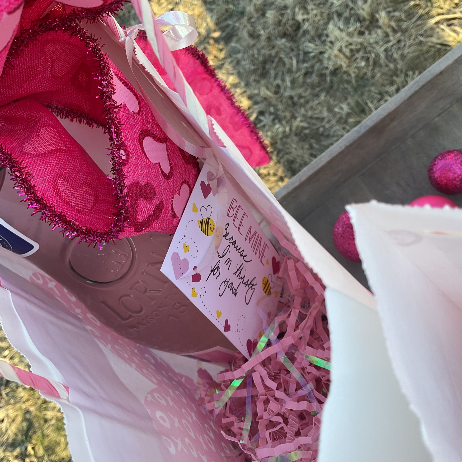 Pink tinsel-edged bow with heart details and an enclosure card attached to a gift bag