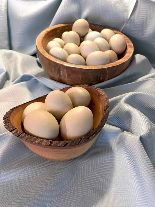 Two wooden bowls filled with light brown eggs on a light gray fabric background