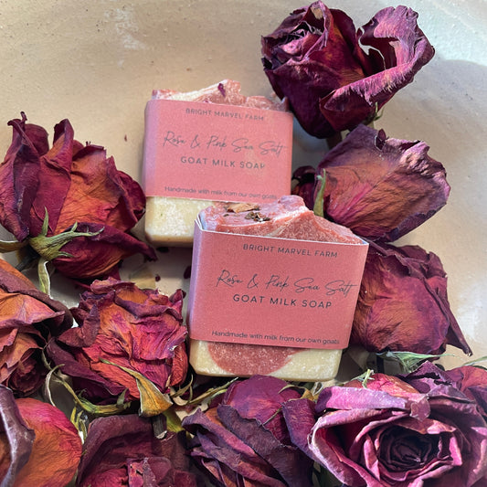 Two bars of soap surrounded by dried red roses in a white bowl.