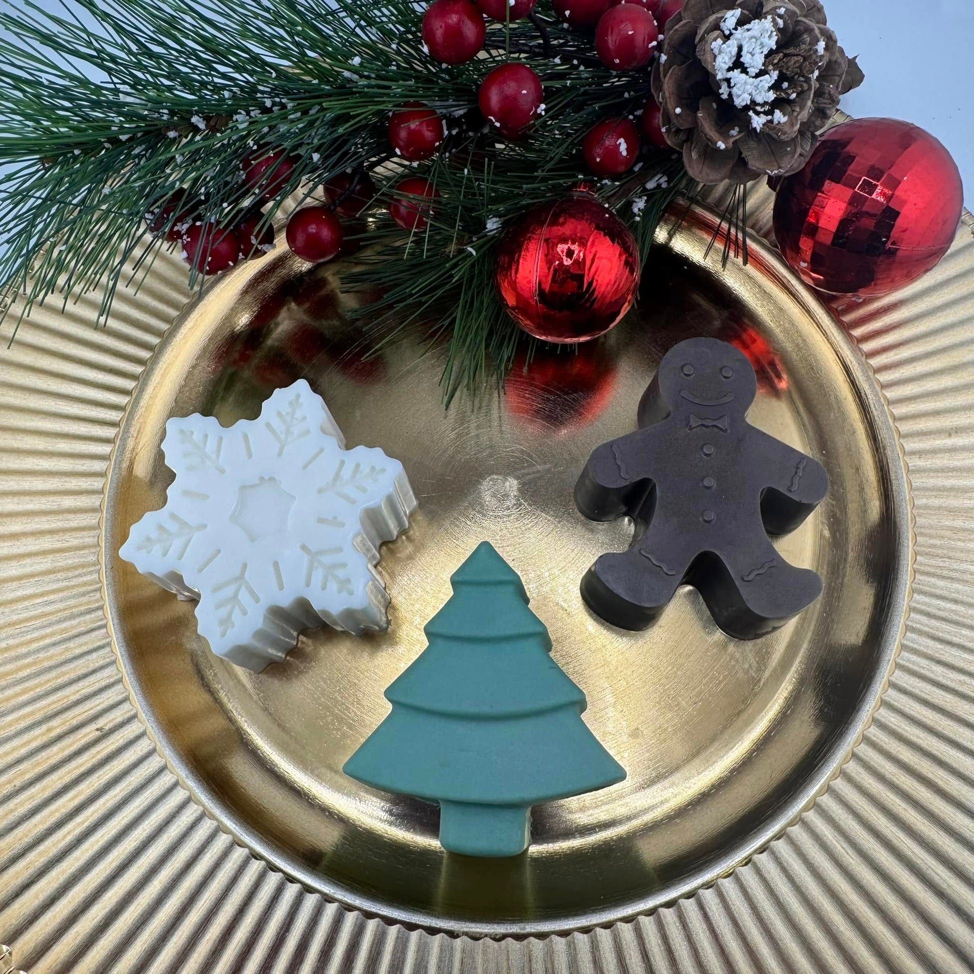 Three Christmas-themed soaps on a gold plate with festive decorations.