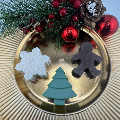 Three Christmas-themed soaps on a gold plate with festive decorations.