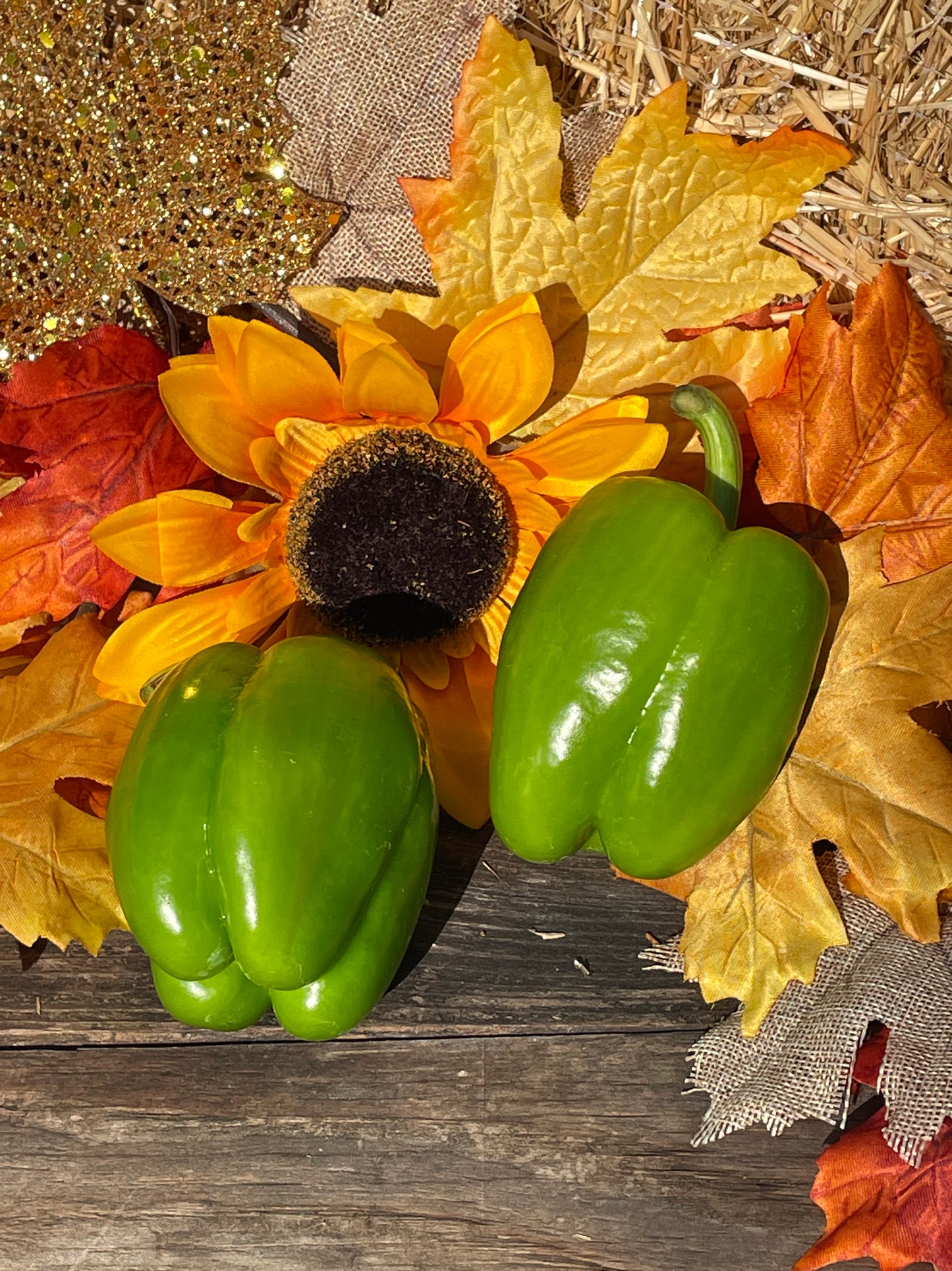 Decorative arrangement with fresh green bell peppers on a sunflower and autumn leaves on a wooden surface