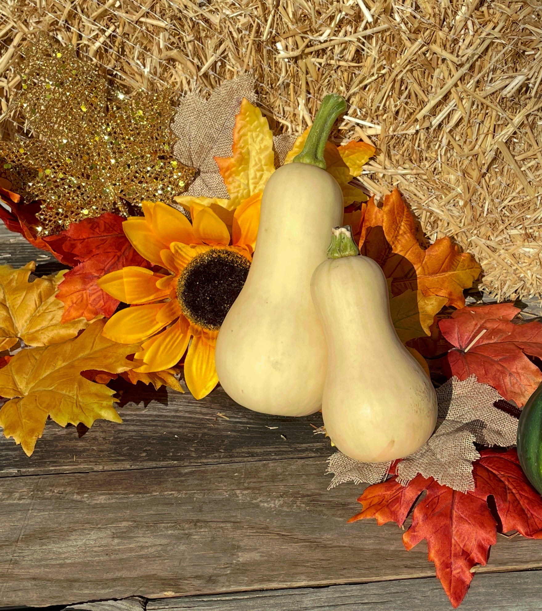 Two white gourds on a wooden surface with autumn leaves and sunflower decorations.