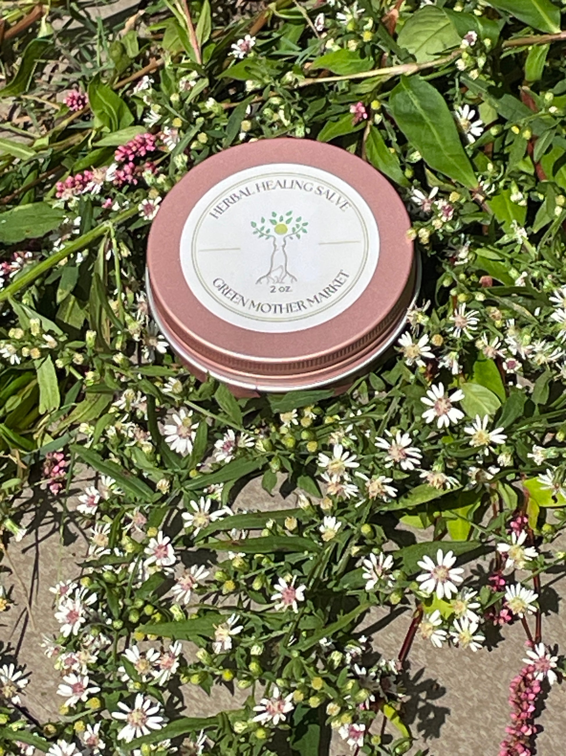 Tin of herbal salt on a bed of green leaves and white flowers