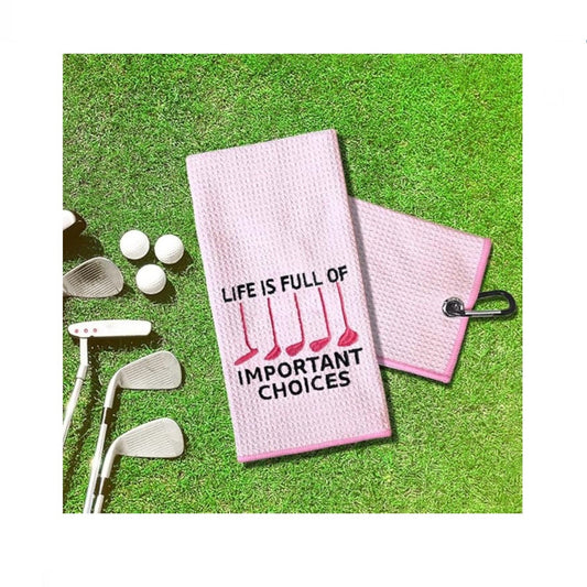 Pink golf towel with 'Life is full of important choices' text on grass with golf clubs and balls.