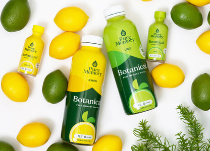 Pure Memory Botanical drinks in lemon and lime flavors surrounded by lemons, limes, and greenery on a white background. A sprig of fresh rosemary peeks from the bottom right.