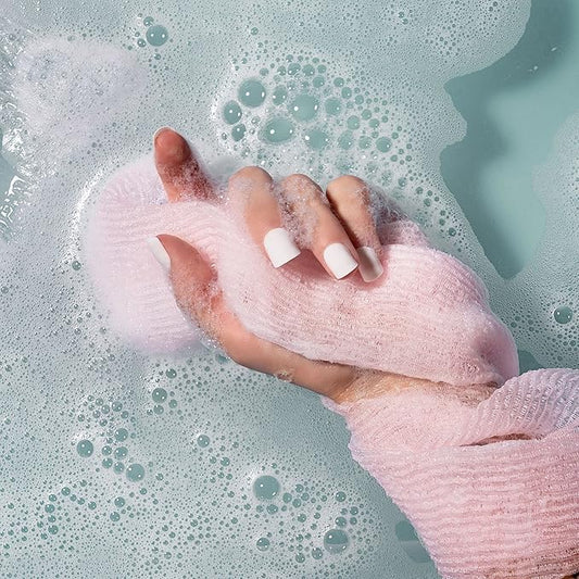 Hand with pink bath scrubber in a bathtub filled with bubbles