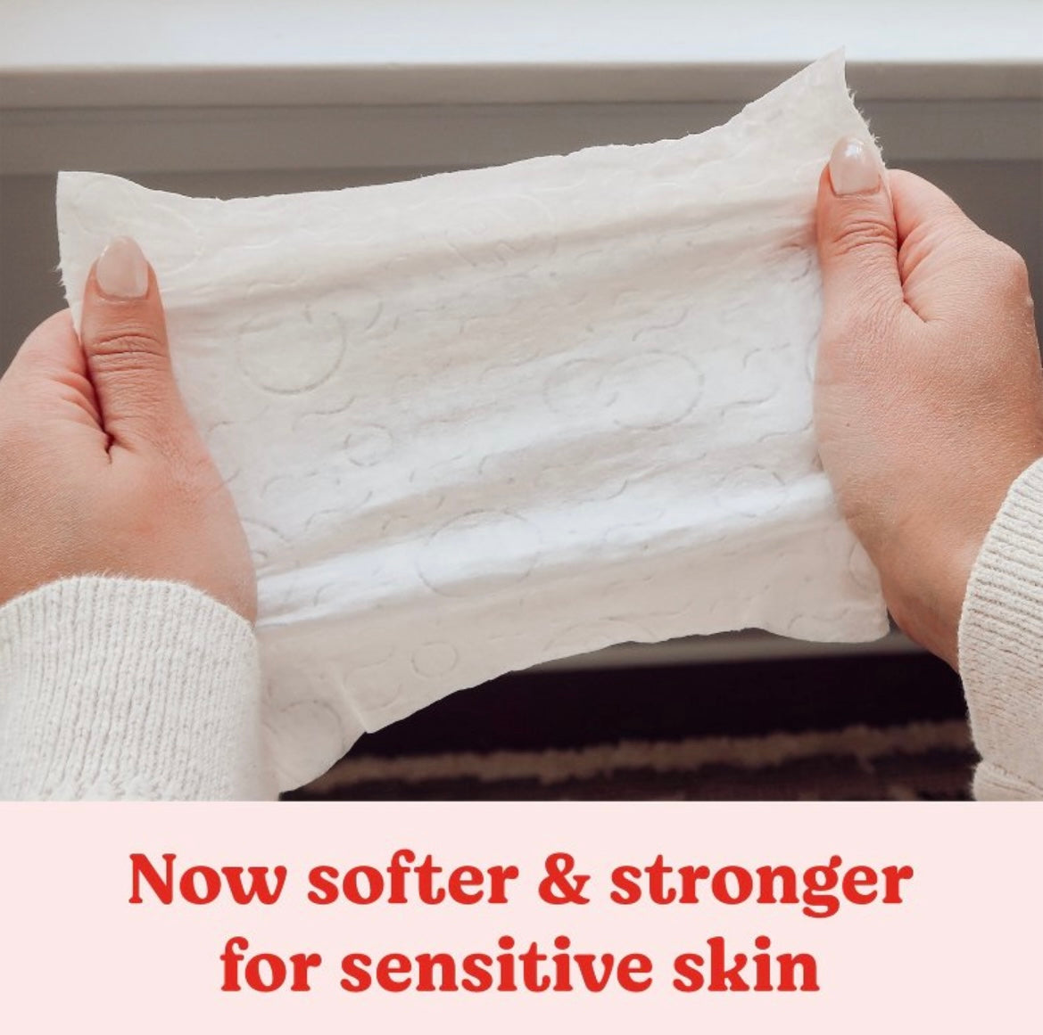 White fabric held by hands with text 'Now softer & stronger for sensitive skin' on a neutral background