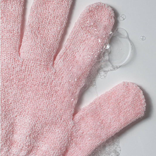 Pink exfoliating glove with soap suds on a light gray background