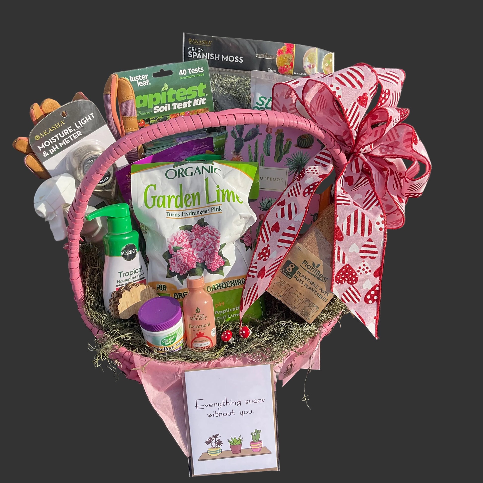 Gardening gift basket with long  handle and various gardening supplies on a dark gray background.  A card sits in front with a succulent plant pun!